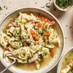 A bowl of chicken tortellini soup with chopped vegetables and herbs.