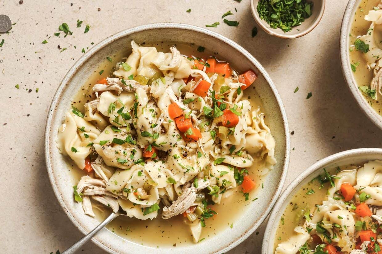 A bowl of chicken tortellini soup with vegetables and herbs.