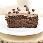 A slice of chocolate cake with frosting and chocolate chips on a white plate.