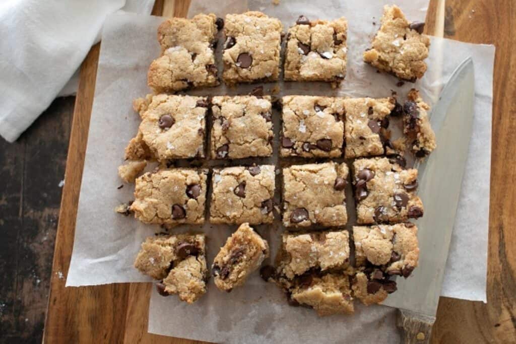 Freshly baked chocolate chip blondies cut into squares on parchment paper.
