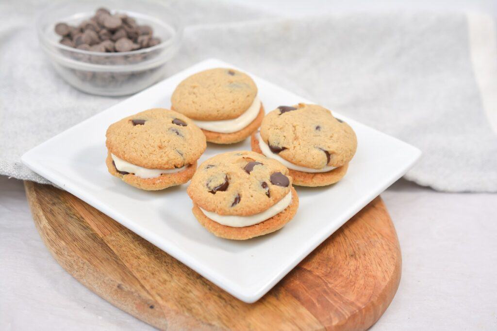 Chocolate chip cookies with cream filling on a white plate.