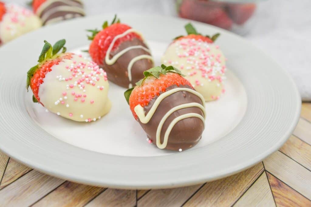 Chocolate-dipped strawberries with various toppings on a white plate.