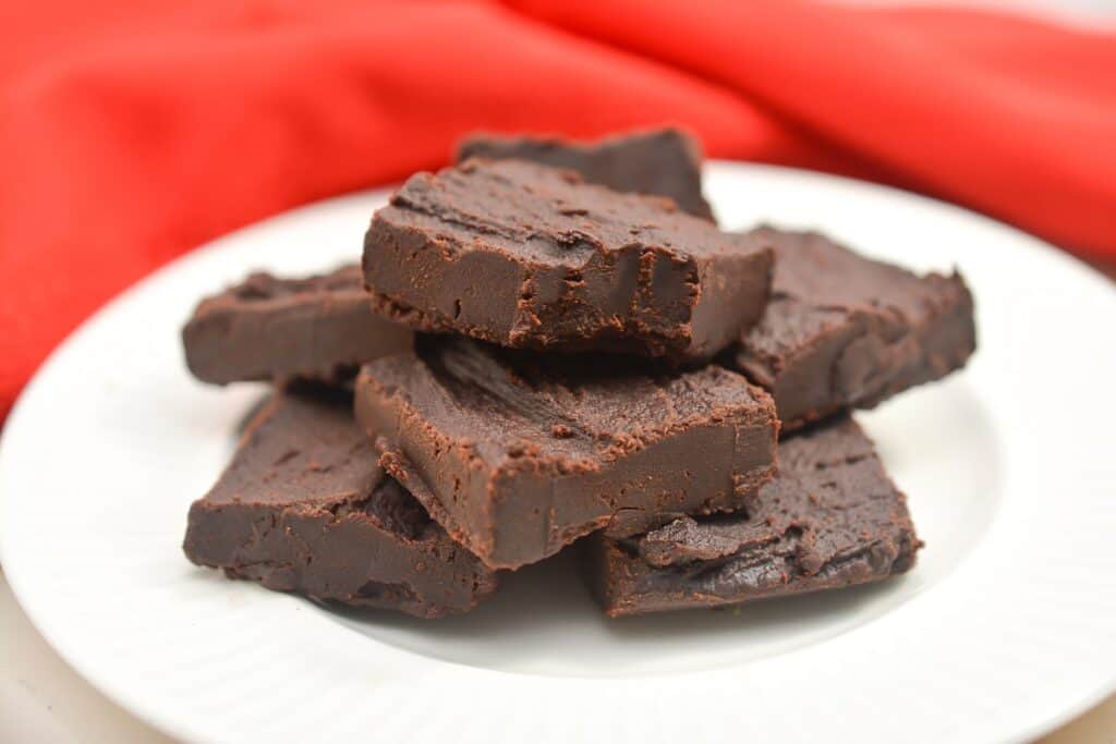 A plate of homemade fudge on a white surface with a red fabric in the background.