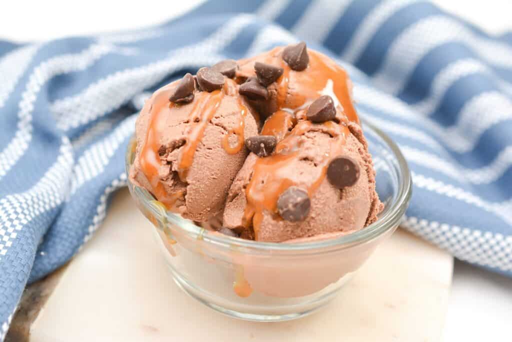Bowl of chocolate ice cream with chocolate chips on a white surface with a blue and white striped napkin.