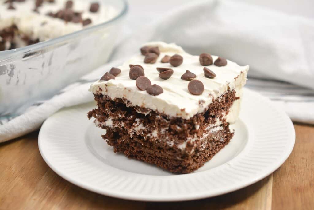 A slice of chocolate cake with white frosting and chocolate chips on a white plate.