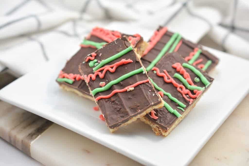 Homemade chocolate-covered biscuit bars with red and green icing on a white plate.