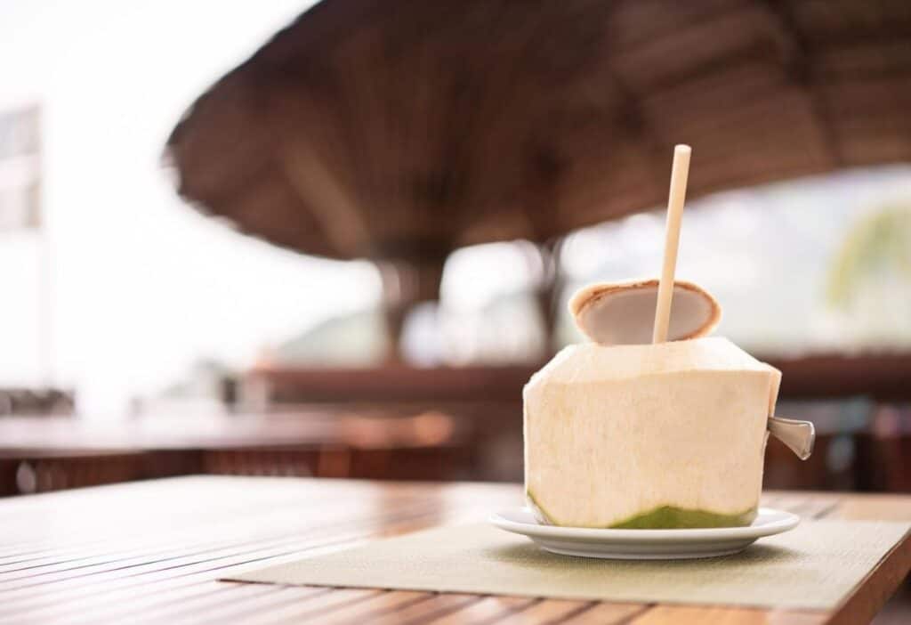 A coconut drink with a straw sitting on a wooden table.