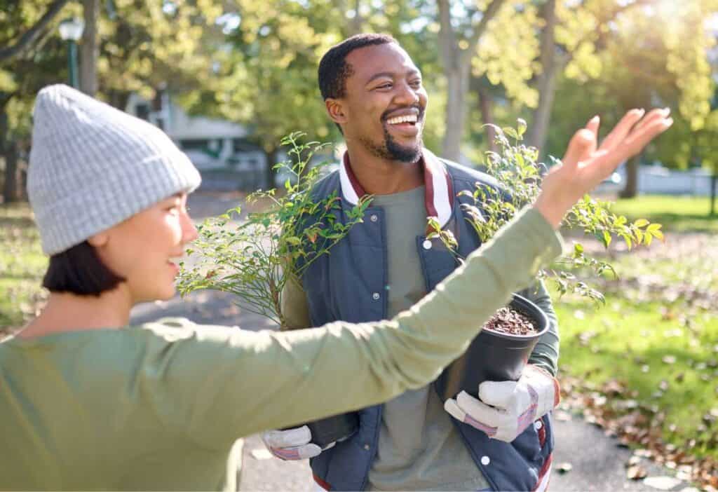 Two people smiling and engaging in a gardening activity outdoors on a sunny day.