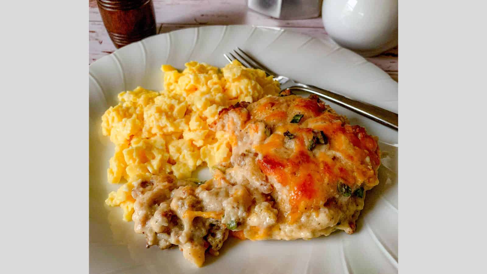 A plate loaded with biscuit and sausage gravy casserole and scrambled eggs.
