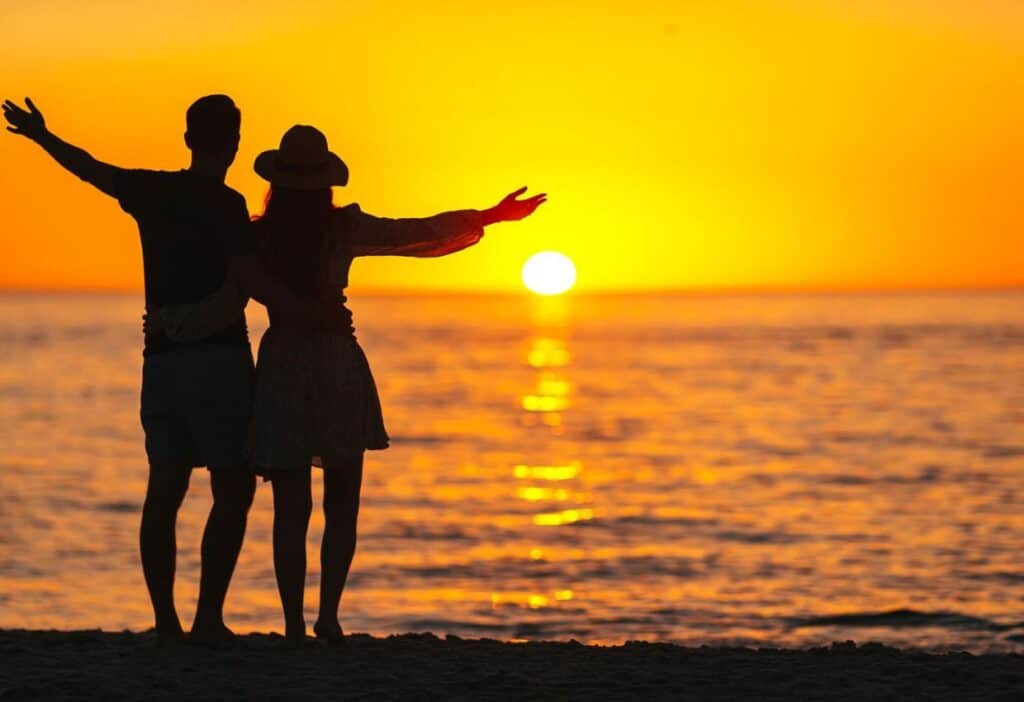 A couple is standing on the beach at sunset.