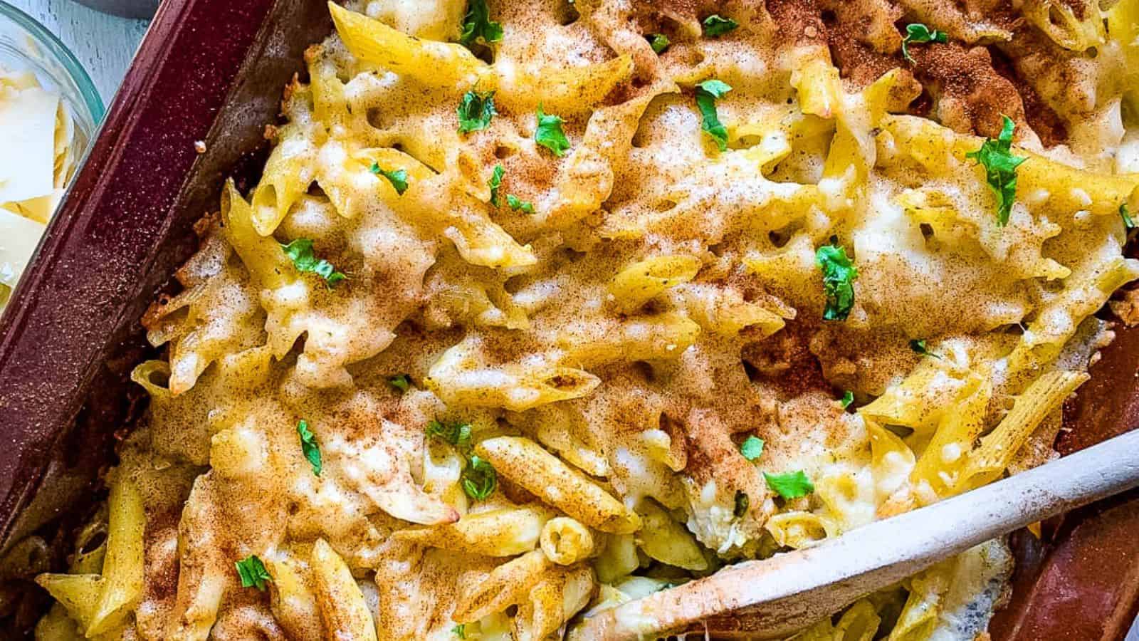 Penne and chicken in a casserole dish with pesto and cheese.