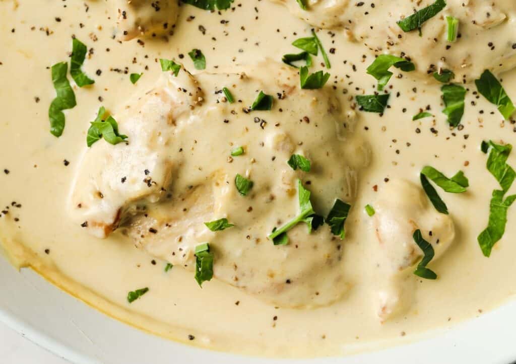 Creamy chicken dish garnished with herbs and black pepper.