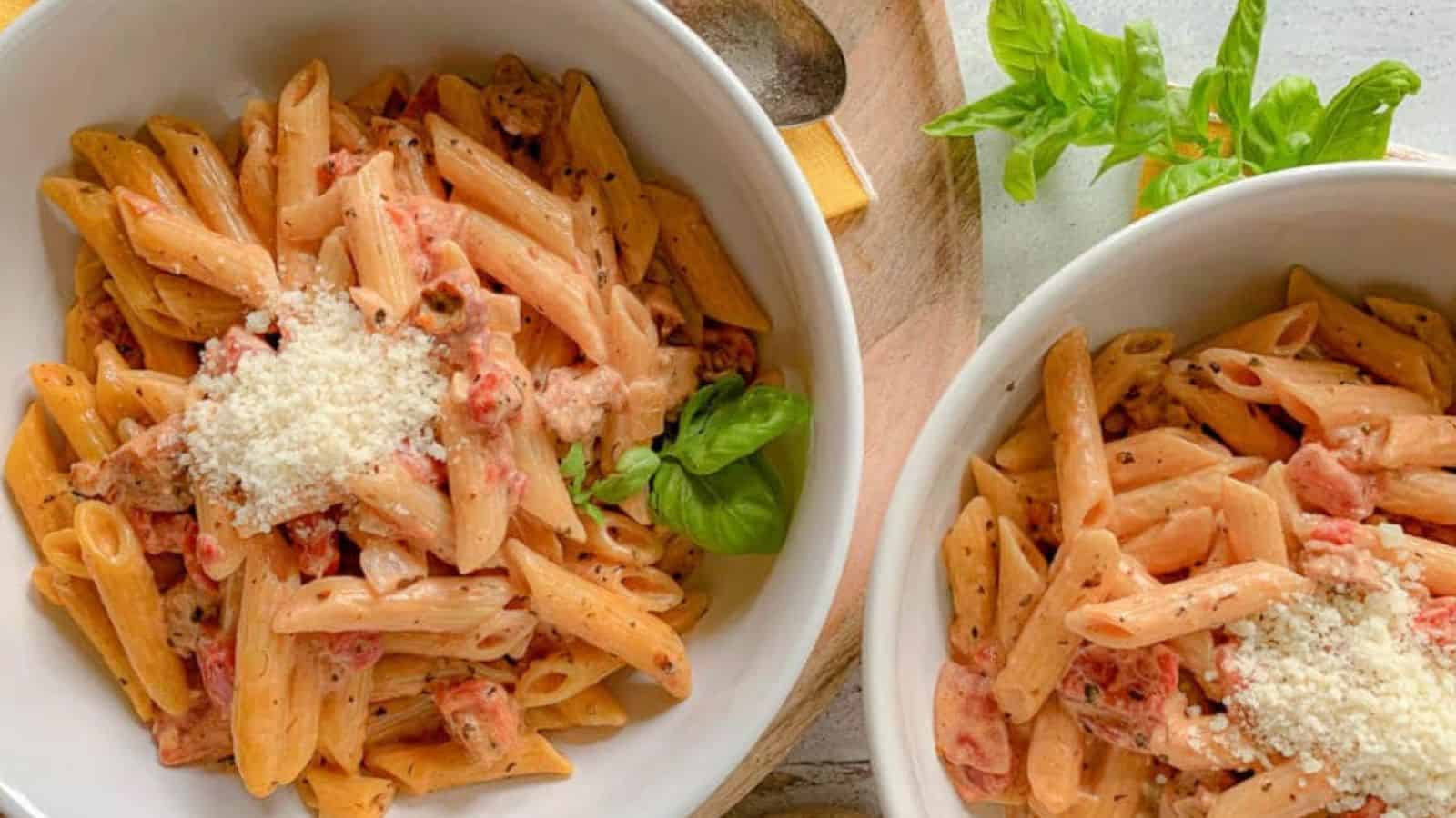 Two pasta bowls filled with penne and chunks of sausage and tomatoes.
