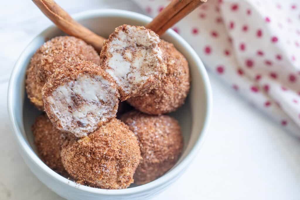 A bowl of cinnamon sugar-coated doughnut holes with one bitten to reveal the inside.