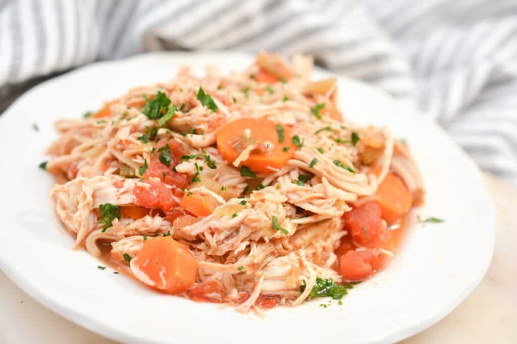 A plate of shredded chicken with tomatoes and herbs.