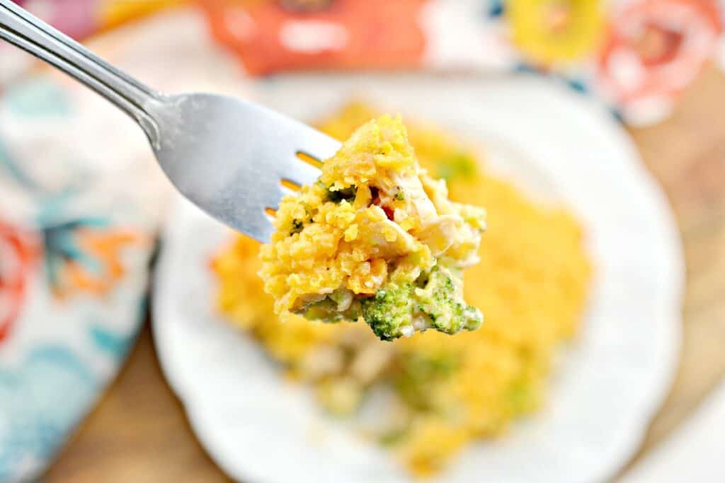 A close-up of a fork holding a bite of broccoli and cheese casserole, with a plate of the casserole in the background.