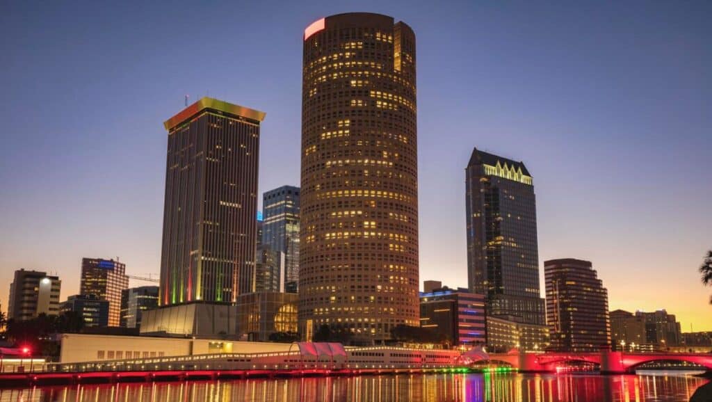 City skyline at dusk with illuminated skyscrapers and a lit bridge over a river, showcasing things to do in Tampa.