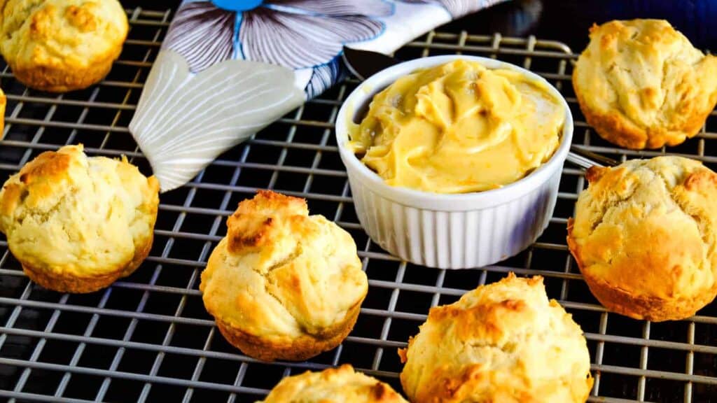 Freshly baked biscuits cooling on a wire rack with a ramekin of honey butter.