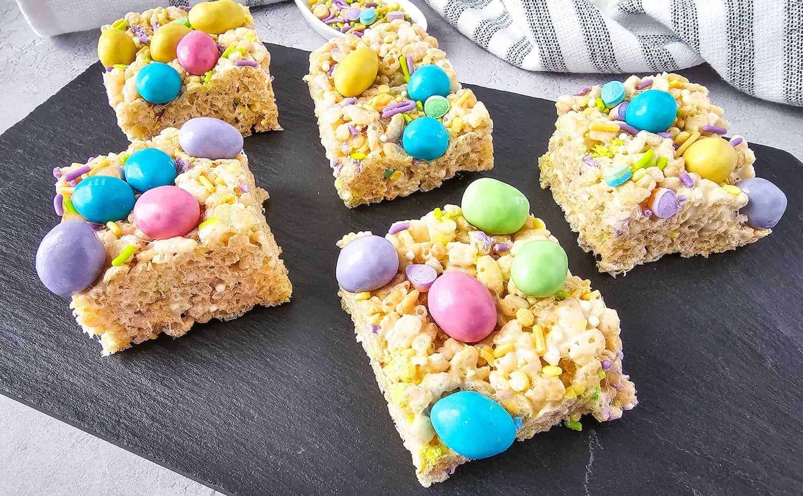 A dark platter displaying rice krispie treats topped with pastel-colored M&Ms.