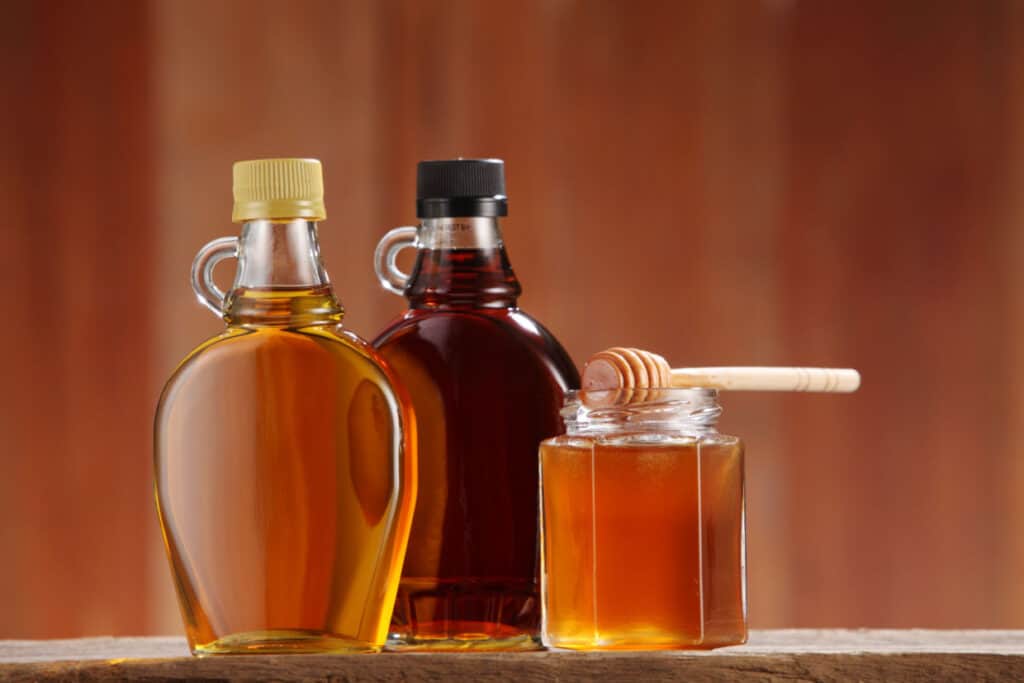 A bottle of honey and a bottle of maple syrup on a wooden table.