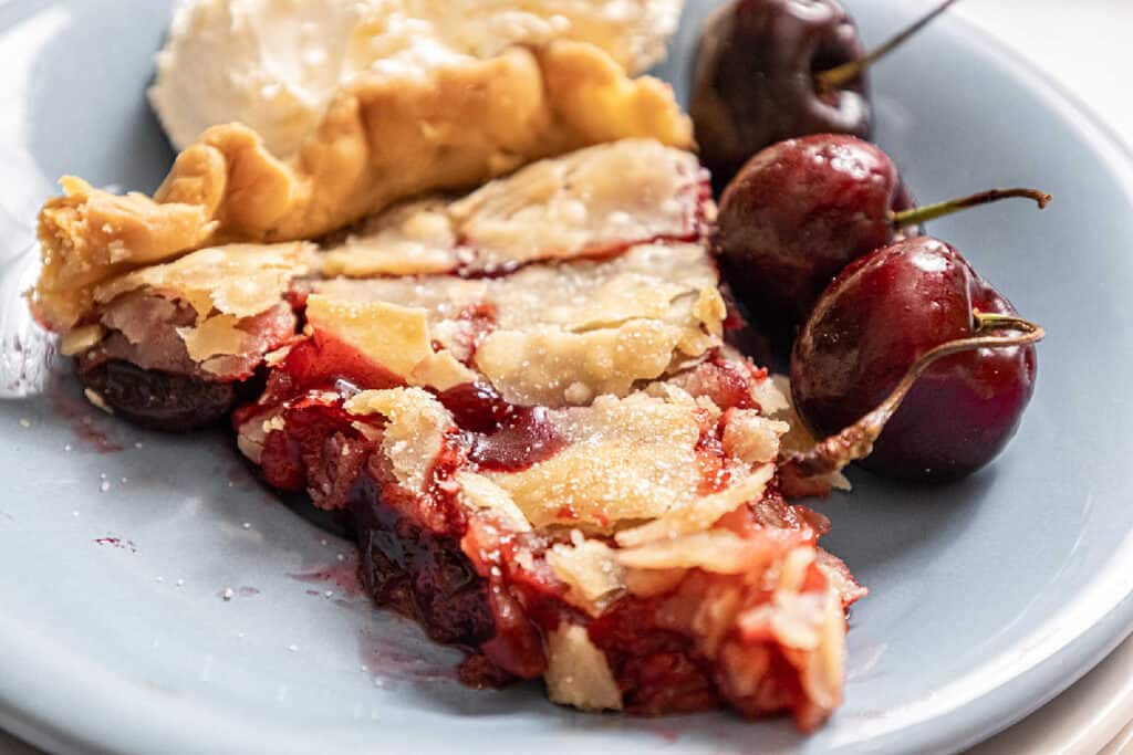 A slice of cherry pandowdy with fresh cherries on a plate.