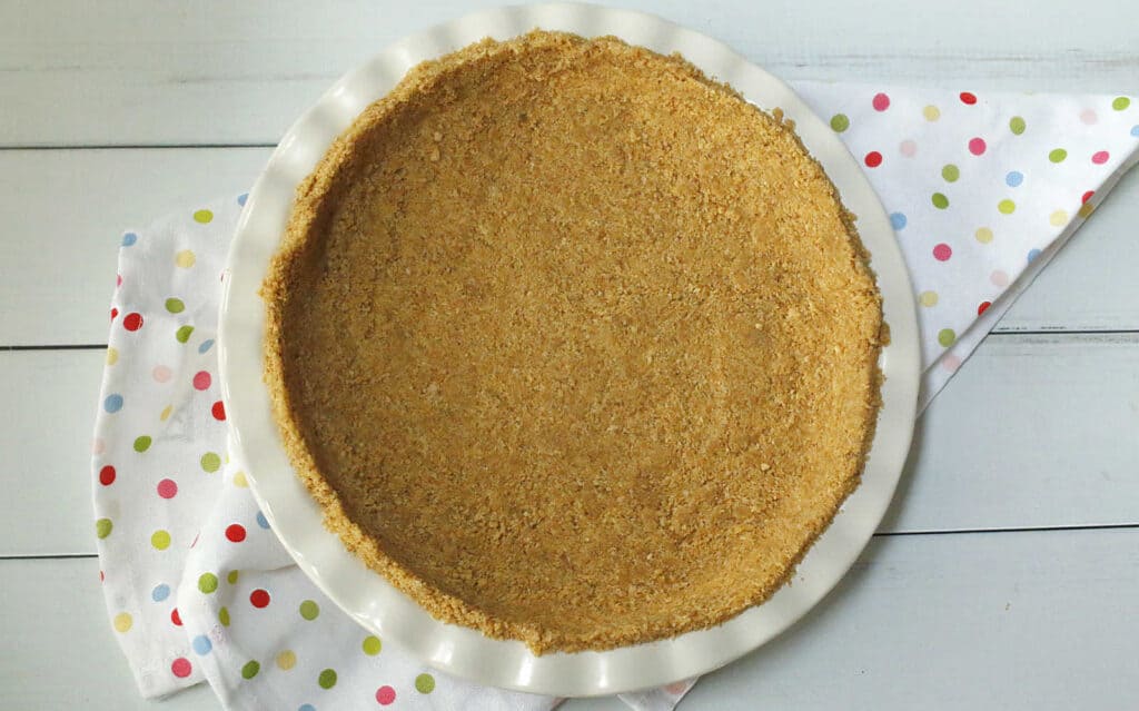 A freshly prepared pie crust on a white plate over a polka-dot napkin.