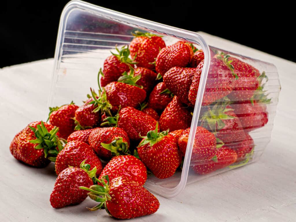 Fresh strawberries spilling from an open plastic container onto a surface.