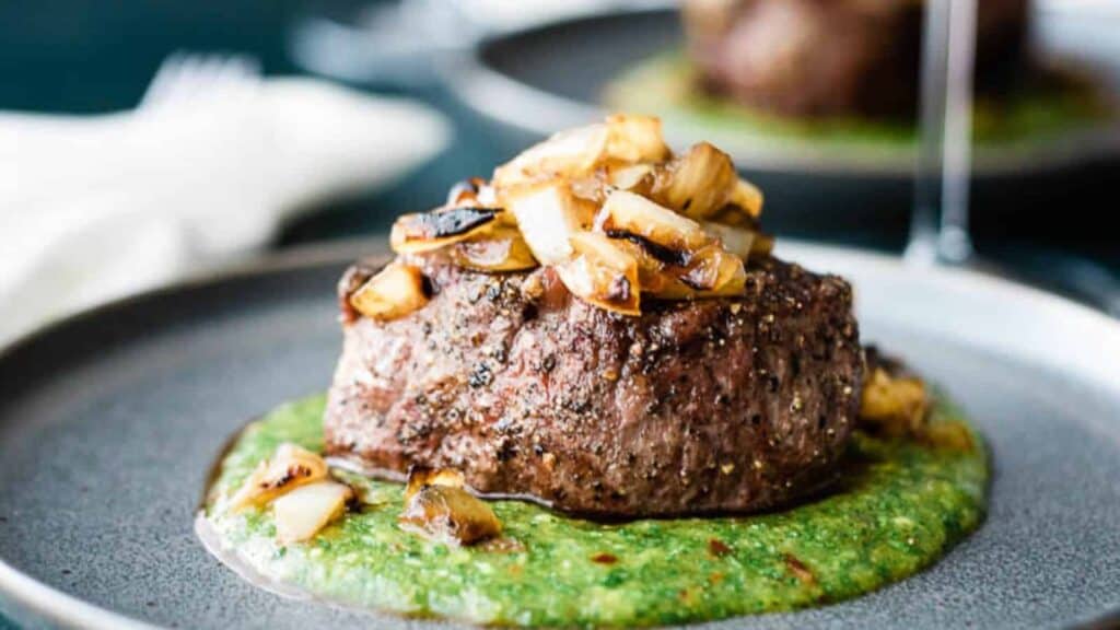 A steak on a plate with green sauce.