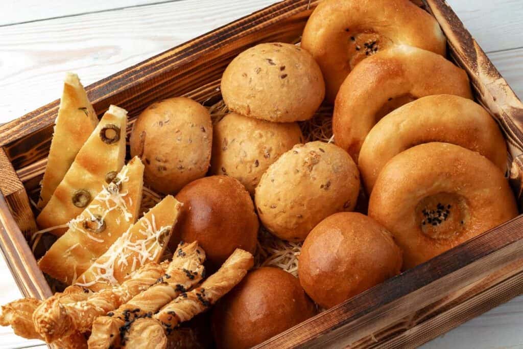 Assorted bread rolls and sticks in a woven basket.