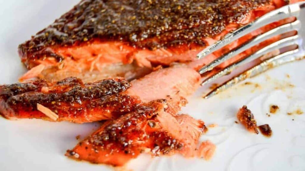 Grilled salmon steak partially flaked with a fork on a white plate.