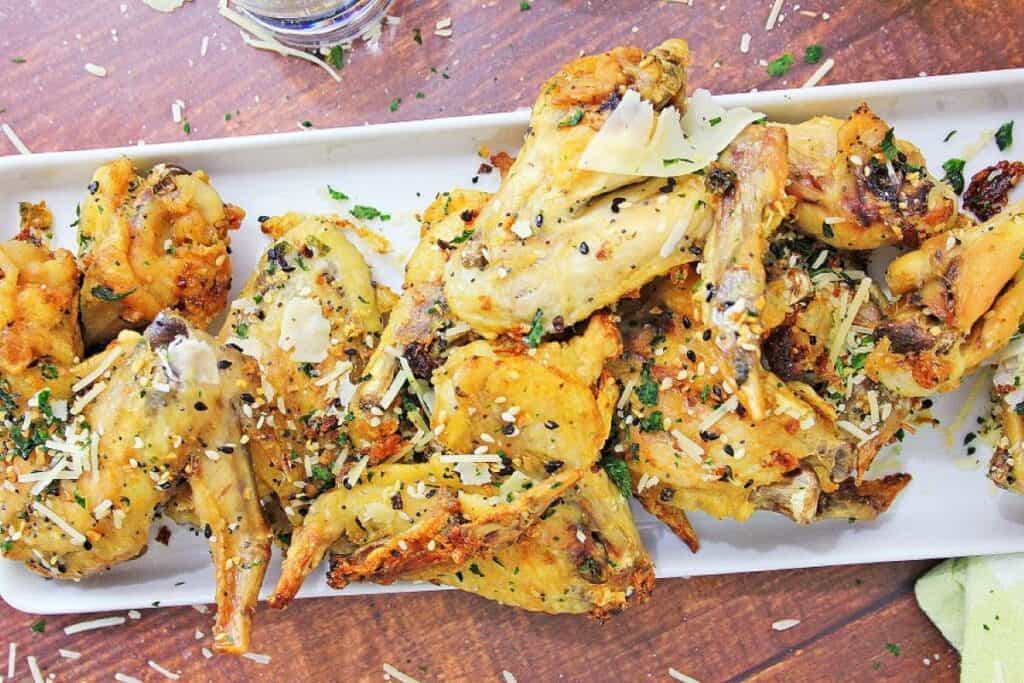 A platter of seasoned chicken wings garnished with herbs and grated cheese.