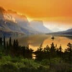 Sunset over a tranquil mountain lake in Montana with vibrant orange skies and silhouetted peaks.