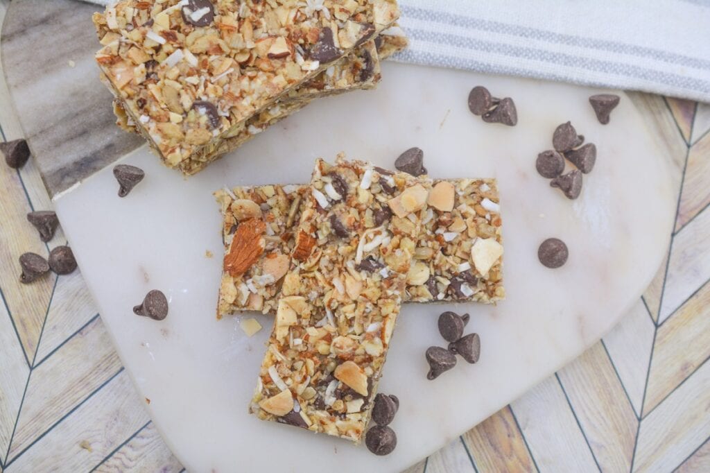 Homemade granola bars with nuts and chocolate chips on a marble surface.