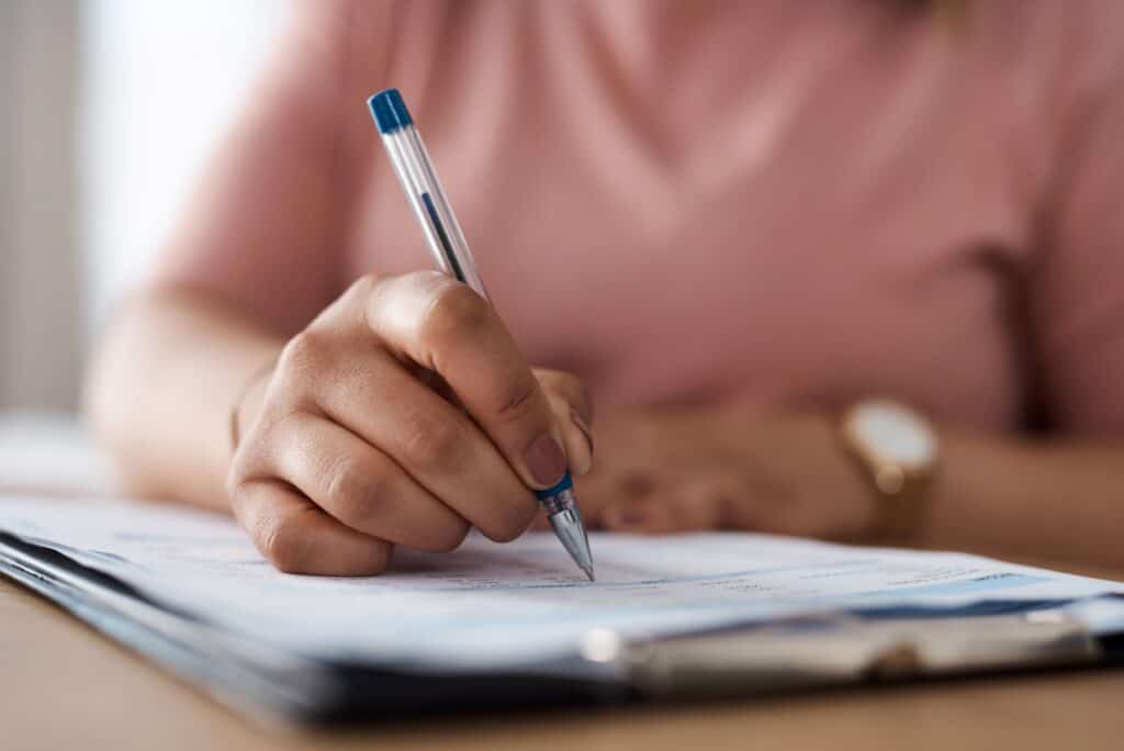 Person writing on a document with a pen.