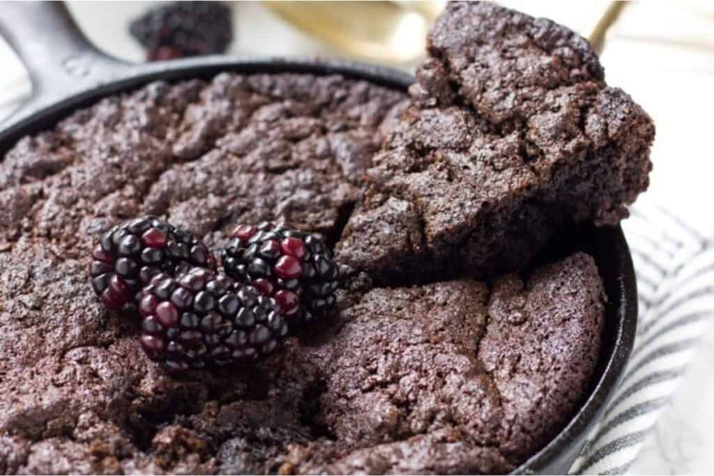 A skillet with freshly baked chocolate cake, topped with blackberries.
