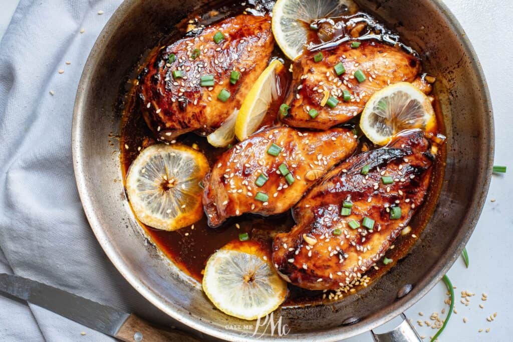 Chicken breasts in a skillet with lemon slices and sesame seeds.