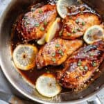 Chicken breasts in a skillet with lemon slices and sesame seeds.