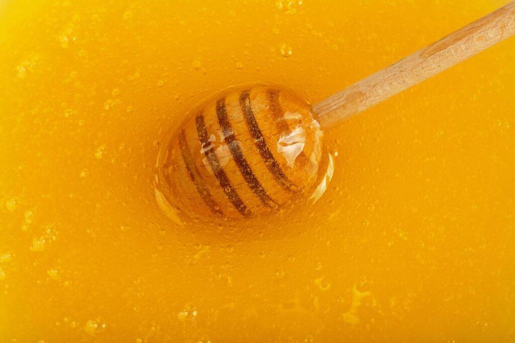 A honey dipper immersed in decrystallized golden honey with visible bubbles around it.