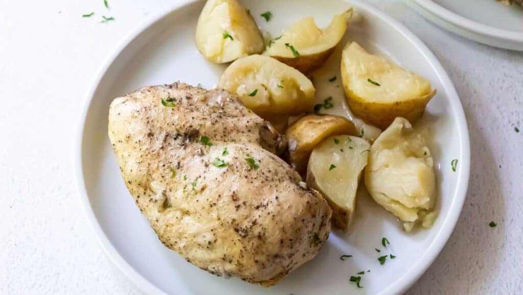 Grilled chicken breast served with roasted potatoes and garnished with herbs on a white plate.