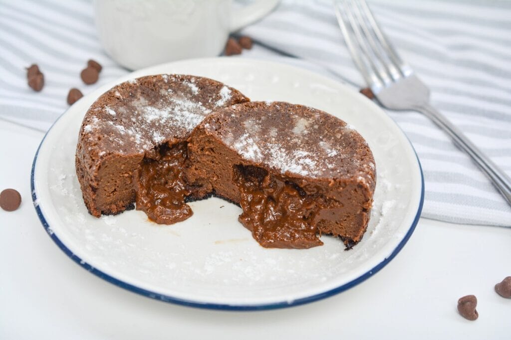 A sliced molten chocolate cake on a white plate with a dusting of powdered sugar.