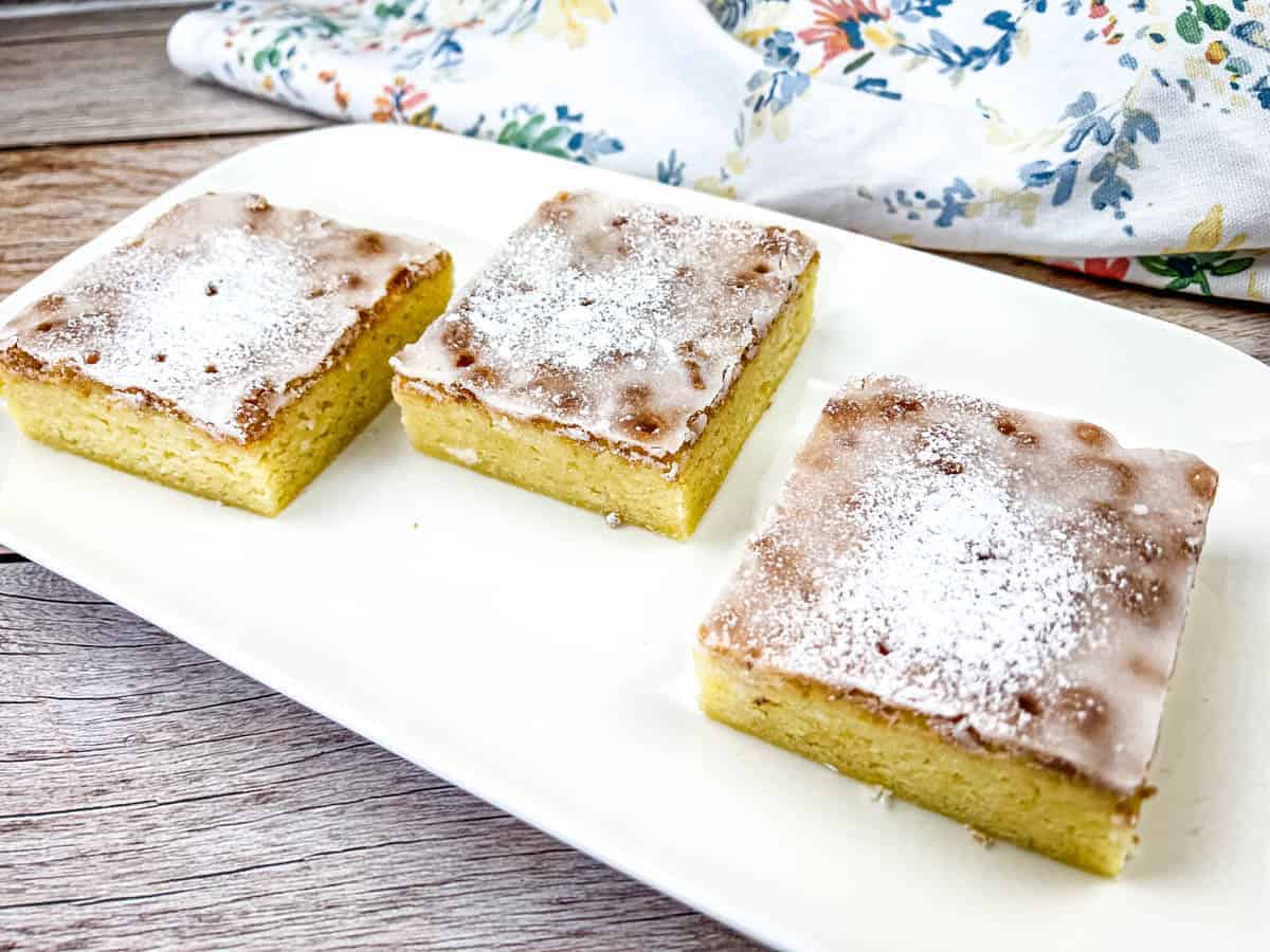 Three square pieces of lemon goldies on a white plate.