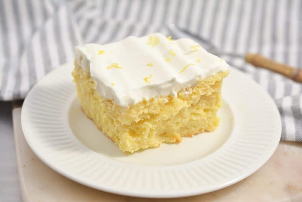 A slice of lemon cake with cream frosting on a white plate.