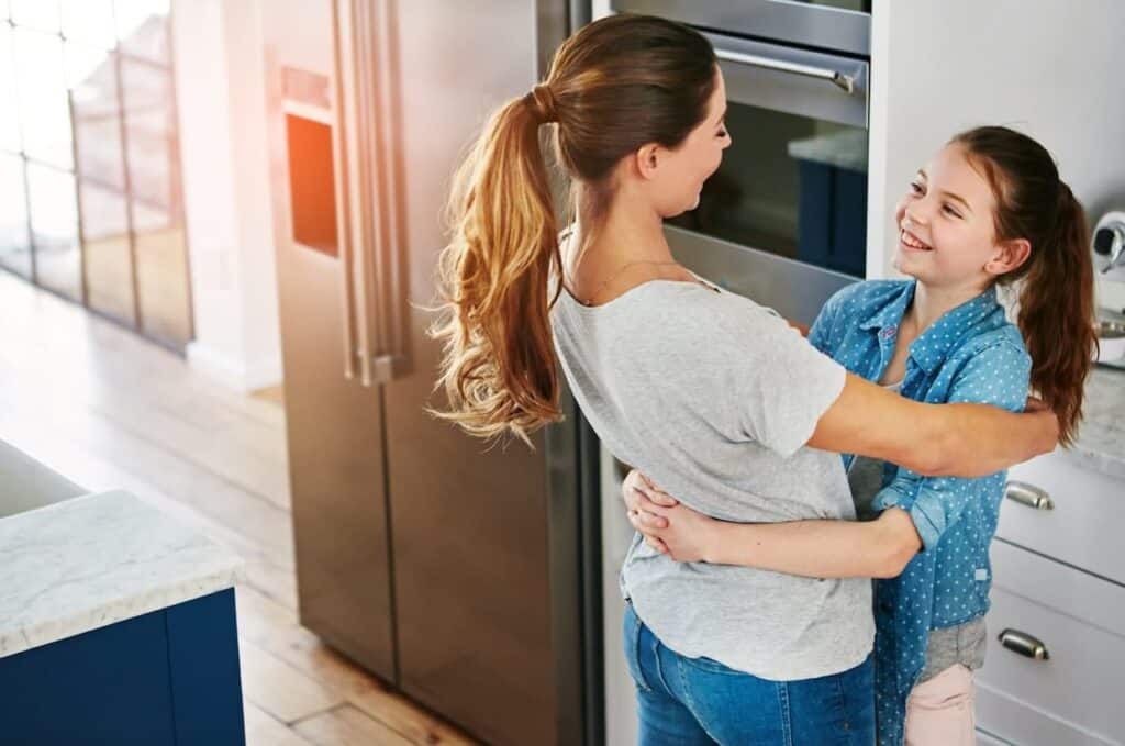 A mother and daughter hugging in the kitchen.