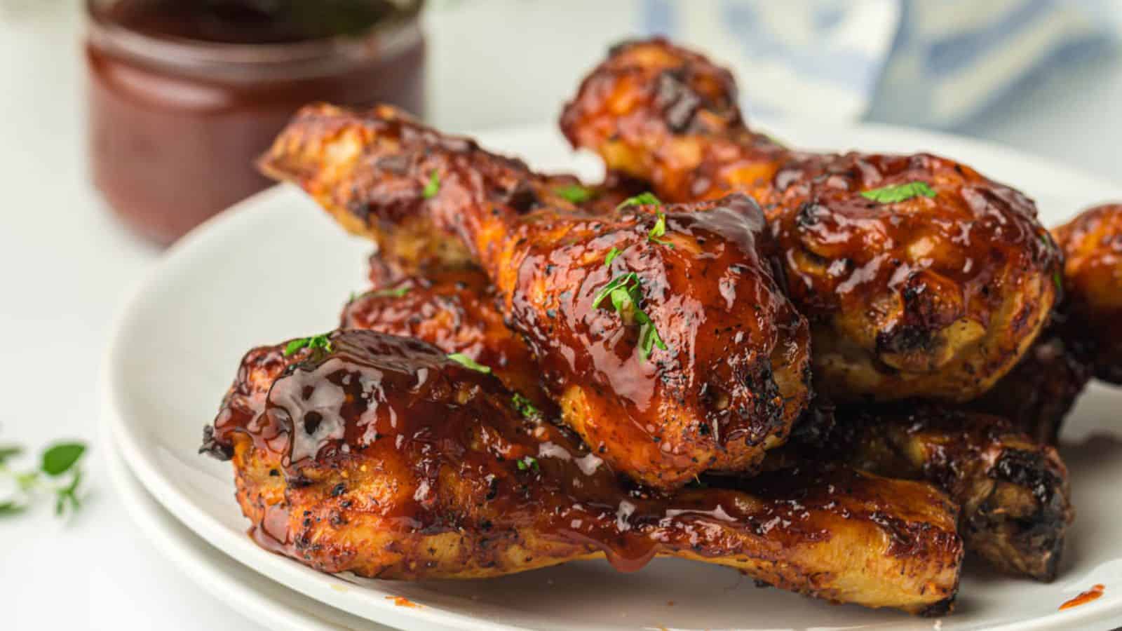 Glazed barbecued chicken drumsticks on a white plate.