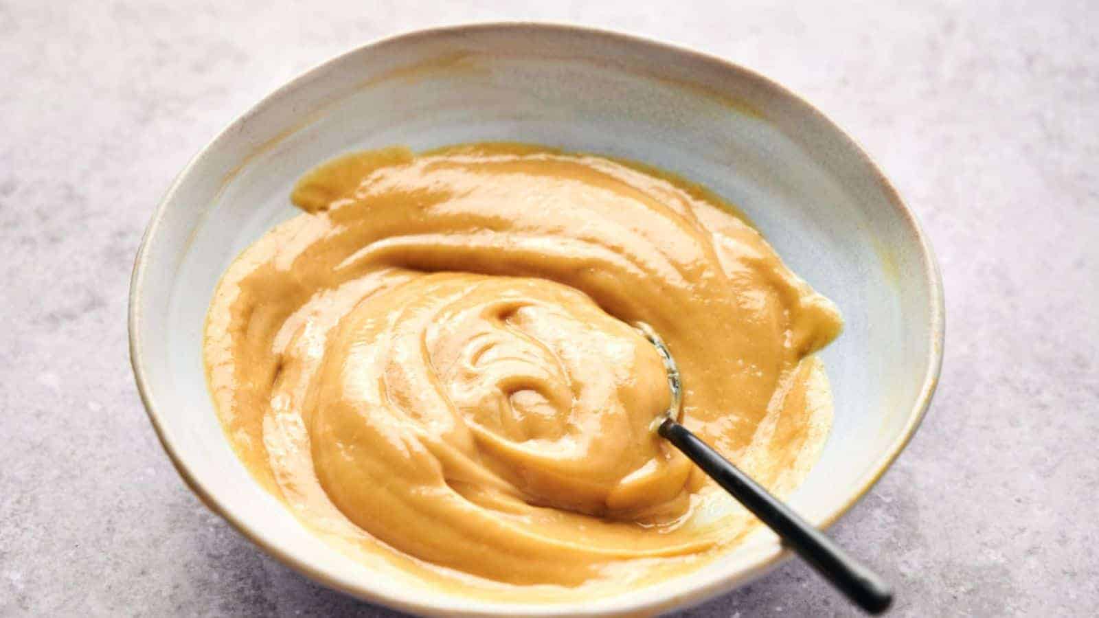 A bowl of smooth, creamy peanut butter with a hint of Chick-fil-A sauce and a spoon inside.