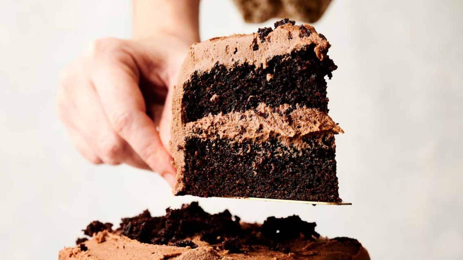 A person holding a slice of chocolate layer cake with frosting from a chocolate cake recipe.