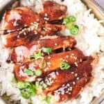 Bowl of rice topped with glazed chicken and garnished with green onions and sesame seeds.