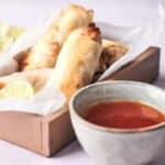 A tray of spring rolls accompanied by lime wedges and a bowl of dipping sauce.