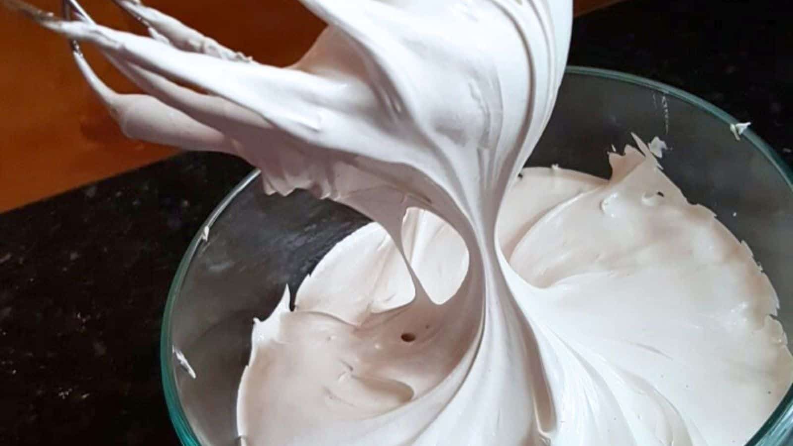 Image shows Stiff peaks of homemade marshmallow fluff being lifted from a glass bowl.