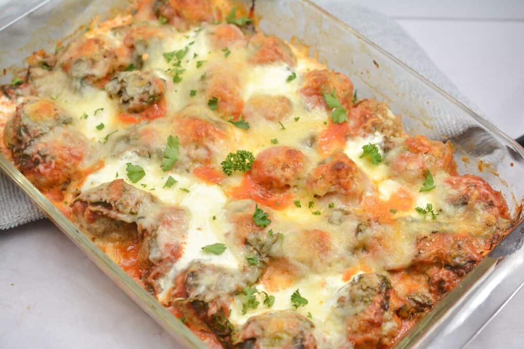 A tray of baked meatballs topped with melted cheese and garnished with fresh herbs.